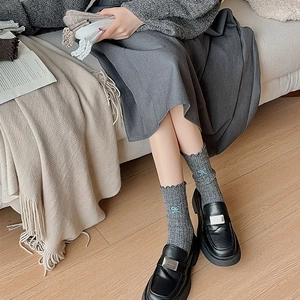 Detail of wool socks with ruffles and blue bow embroidery paired with black loafers