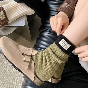 Détail de chaussettes en laine vert olive avec étiquette décorative et bord noir