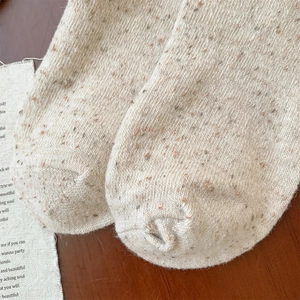 Close-up of thick beige wool knit socks featuring colorful nep yarn texture and soft fabric