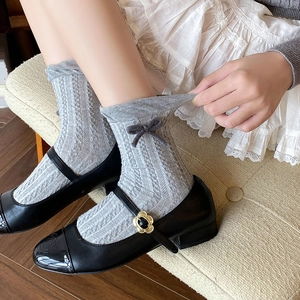 Grey cable-knit mid-calf socks with dark grey bows paired with black Mary Jane shoes