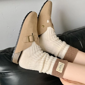 Détail de chaussettes en laine bicolores avec étiquette et mules en daim marron