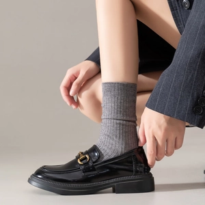 Close-up of black glossy loafers with gold horsebit and striped wool socks
