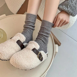Detail of grey cable knit wool socks paired with cozy white fleece lined mule slippers