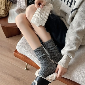 Close-up of thick rib-knit dark gray wool socks worn with plush slippers in a cozy room