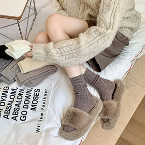 Thick wool cable knit socks paired with plush open-toe slippers in warm earth tones