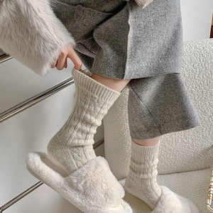 Close-up of white cable-knit wool socks featuring thick textured patterns and soft fur slippers