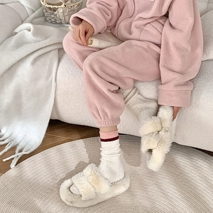 Détail du pyjama en polaire rose et des chaussons en peluche sur un tapis en tricot