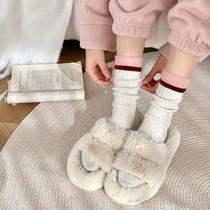 Détail de chaussettes en laine à rayures rouges et de pantoufles en peluche beige chaud