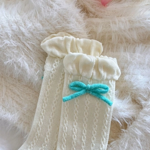 Close-up of off-white knit socks with lace cuffs and blue 3D bow detail and cable pattern