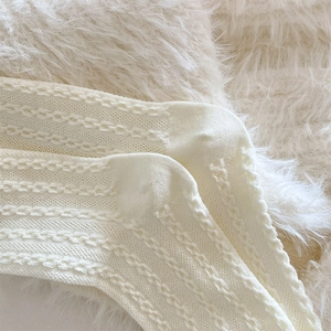 Close-up of white knitted socks featuring intricate cable stitch patterns and textures