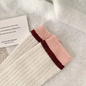 Détail de chaussettes en laine à côtes crème avec revers rayés bordeaux et rose doux
