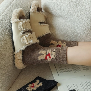 Close-up of beige plush slippers with brown socks featuring cute embroidered bear detail