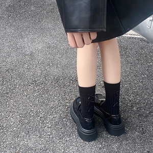 Detail of black platform loafers with bows on mid-calf socks for academic style