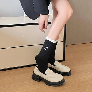 Detail of black mid-calf socks with white bow embroidery styled with beige loafers