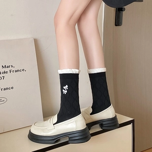Detail of black crew socks with white bow embroidery and ruffled cuffs worn with loafers