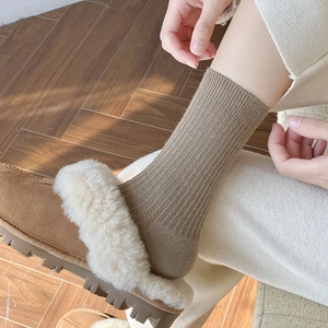 Close-up of brown ribbed wool socks paired with plush slippers on wood floor
