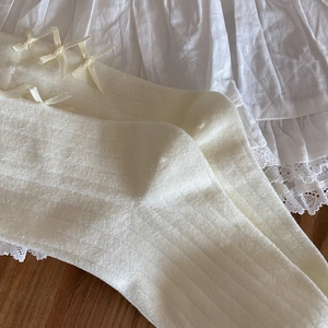 Close-up of white ballet-style socks with satin bow and delicate lace trim details