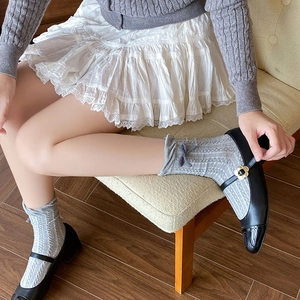 Close-up of grey knitted socks with delicate bow details and black Mary Jane shoes