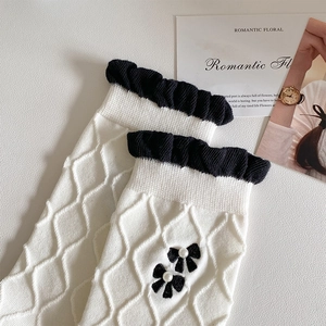 Detail of white argyle knit socks featuring black bow ties with pearls and ruffle cuffs