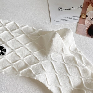Detail of white knit sock with 3D diamond texture and vintage pearl flower accent