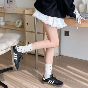 Gros plan de baskets en cuir noir portées avec chaussettes à pois et jupe plissée