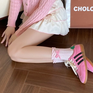 Detail of pink bow socks with ruffled edges worn with suede sneakers and a mini skirt
