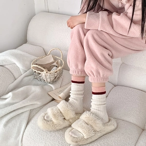 Détail de chaussettes en laine à rayures roses et rouges portées avec des chaussons doux
