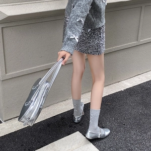 Detail of white ballet-style leg warmers with bows and silver Mary Jane shoes