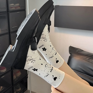 Detail of white crew socks with star and smile patterns worn with black platform loafers