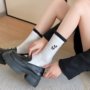 Detail of white argyle knit socks with black ruffle trim and bow decoration