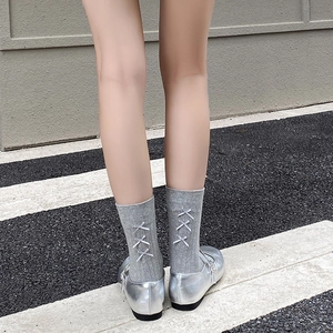 Detail of grey knitted mid-calf socks featuring three satin bows and silver Mary Jane shoes