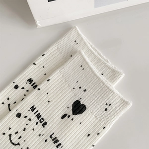 Detailed macro view of white ribbed knit socks with black graffiti heart and smiley prints