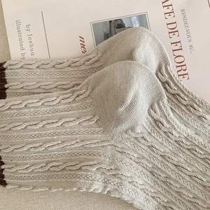 Detailed view of beige cable knit socks with vintage contrast trim on rustic fabric