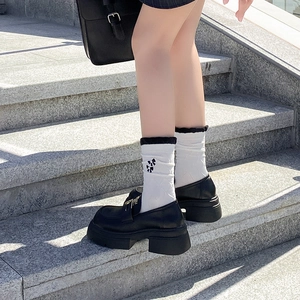 Close-up of white crew socks with black bows and ruffled cuffs paired with loafers