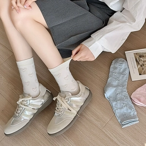 Detailed view of white mid-calf socks with embossed heart texture and retro sneakers