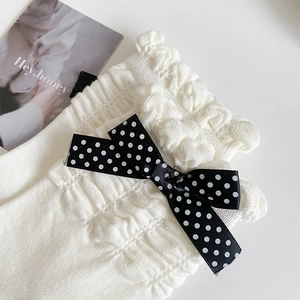 Close-up of white knit ruffle socks featuring cute black polka dot ribbon bows