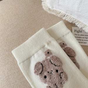 Détail de chaussettes en maille crème avec broderie ours brun floquée en 3D