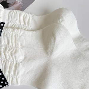 Macro detail of creamy white knit socks with ruffled edges and polka dot bow decoration