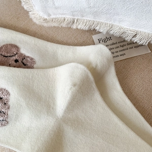 Détail de chaussettes côtelées blanc crème avec motif ours floqué marron et texture douce