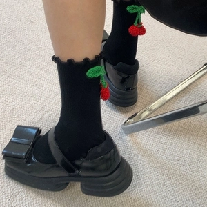 Détail de chaussettes noires à froufrous avec cerises au crochet et chaussures à nœuds