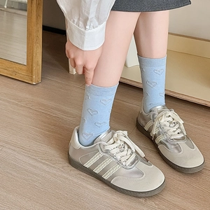 Detail of light blue heart-patterned mid-calf socks paired with gray sneakers on wood floor