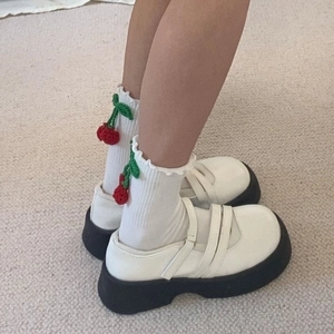 Gros plan de chaussettes blanches à volants avec breloques cerise et chaussures compensées