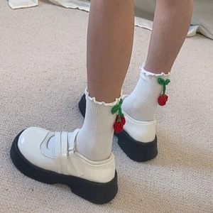 Gros plan de chaussures Mary Jane blanches avec chaussettes au crochet cerise