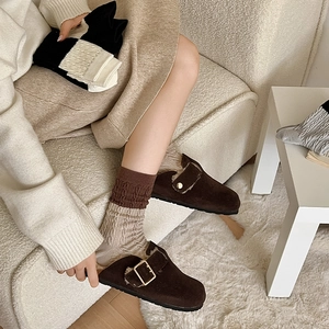 Close-up of brown suede slippers with plush lining and knit socks on white rug