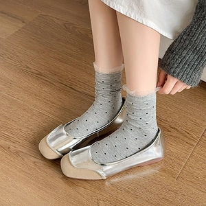 Gray polka dot crew socks with lace trim paired with metallic silver loafers on wood floor