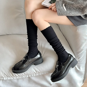 Close-up of black vertical striped knee-high socks paired with patent leather loafers