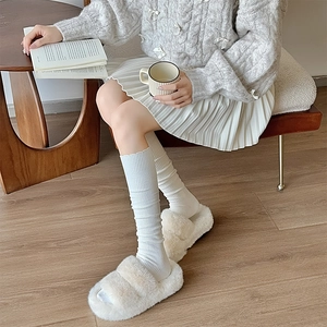 Detail of white ribbed knit long socks paired with plush open-toe slippers for cozy style