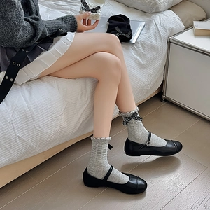 Detail of grey ruffled crew socks with polka dot bows and black Mary Jane shoes