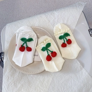 Détail de chaussettes cerise à volants sur une assiette en céramique, texture côtelée