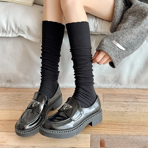 Close-up of black glossy loafers and ribbed knit calf socks worn on wooden floor